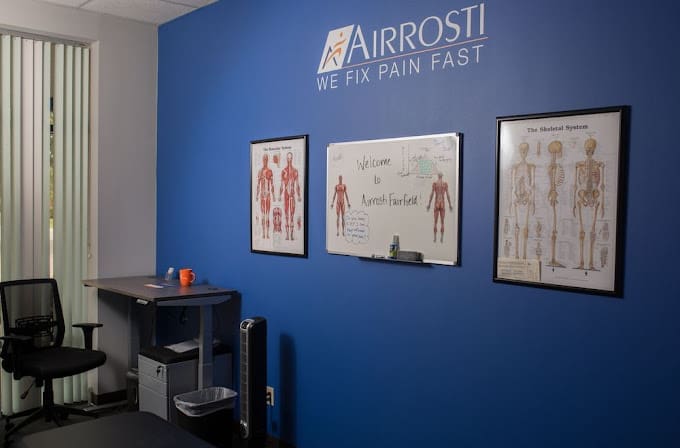 a close up view of the treatment room at Airrosti Fairfield Village. MSK diagrams are featured on the wall as well as the Airrosti logo.