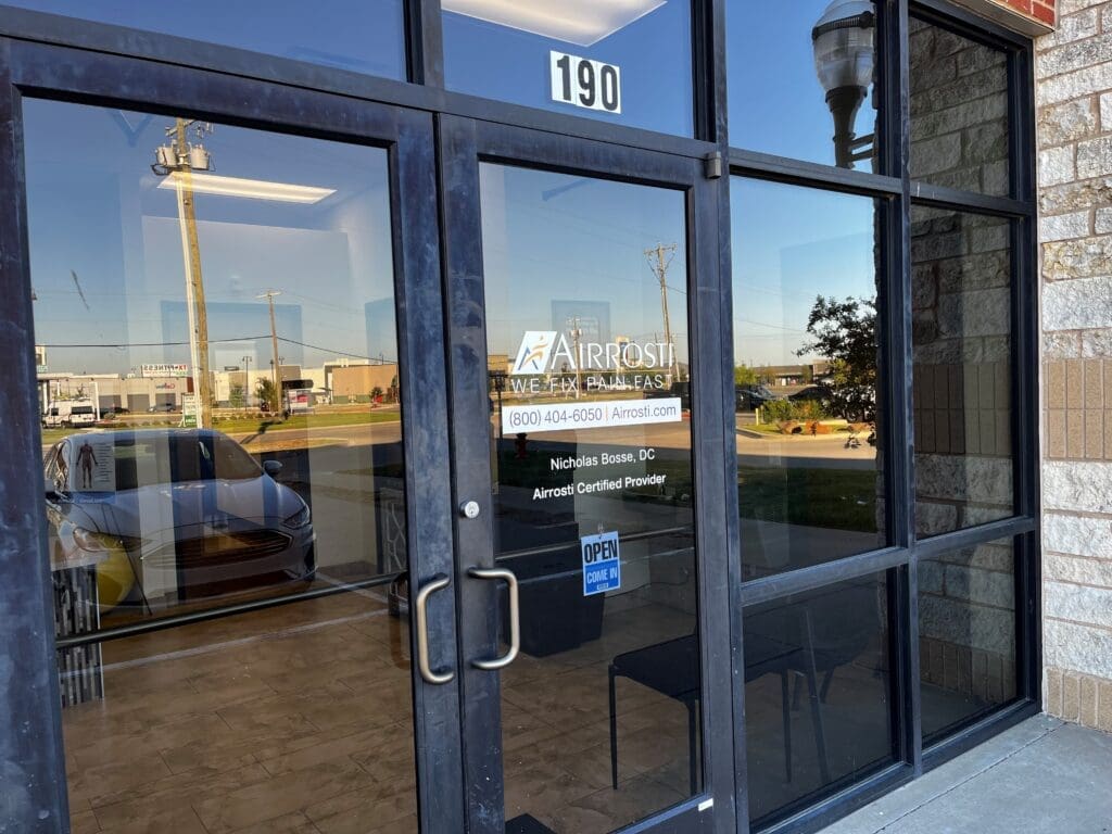 a close up view of the glass door entrance at Airrosti Forney, showcasing the Airrosti branding on the glass doors.