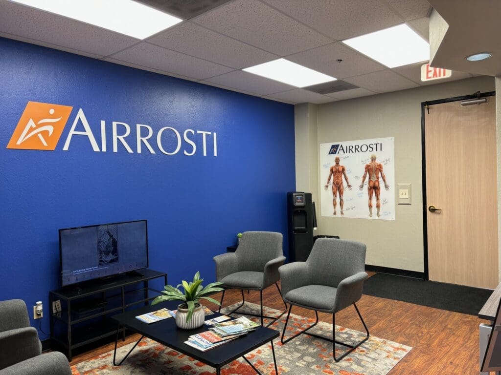 a photo of the lobby at Airrosti Rockwall. Chairs are visible and Airrosti branded posters decorate the walls.