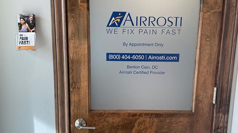 interior entrance door at Airrosti Carrollton. Airrosti logo and provider information is visible on the glass of the door