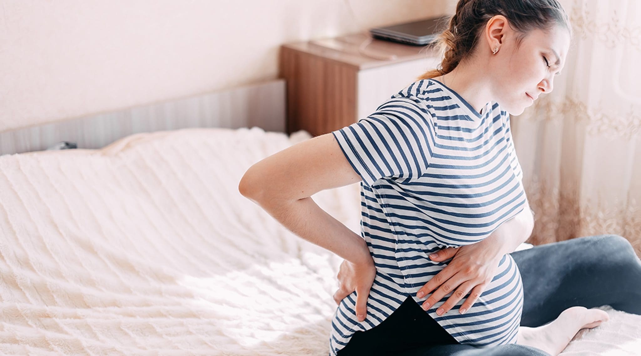 Pregnant woman sitting and holding lower back in pain.