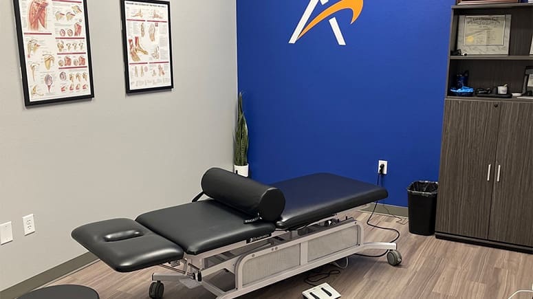 A look inside the treatment room at Airrosti Brownsville, showing a treatment table in the center of the room and musculoskeletal diagrams on the walls.